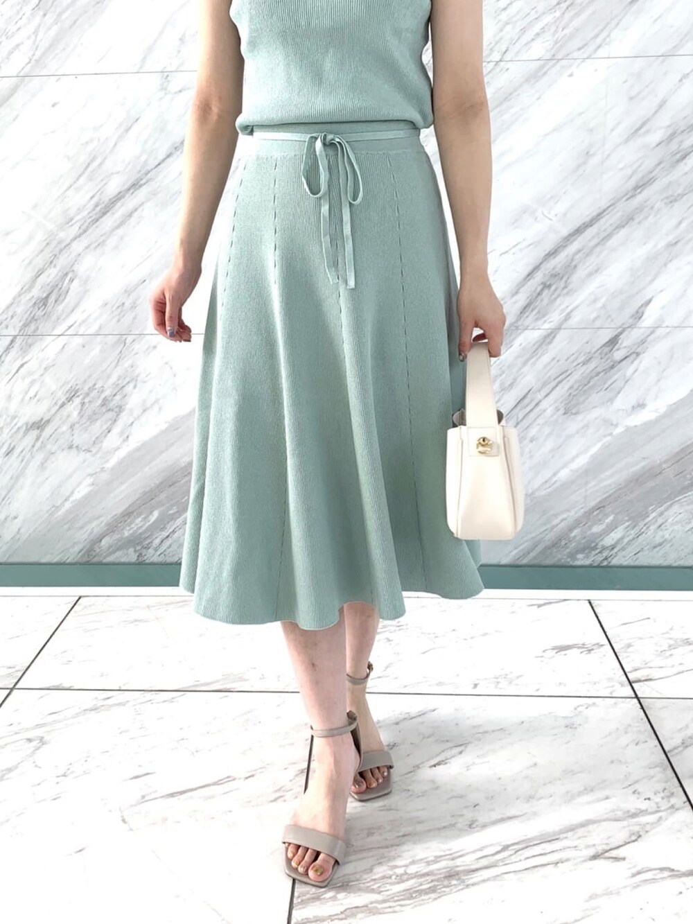 グリーン系のニット/セーター、グリーン系のスカート、グレー系のサンダルを着用したレディースの夏コーディネートの5枚目の写真