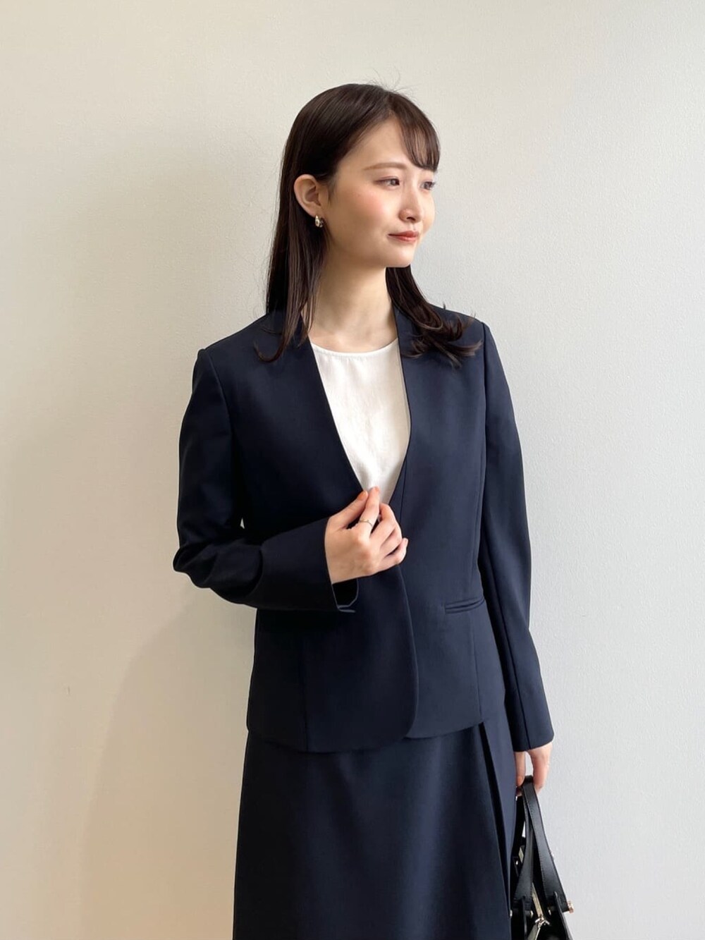 ブラック系のハンドバッグ、ホワイト系のパンプス、ブルー系のノーカラージャケットを着用したレディースの春コーディネートの4枚目の写真