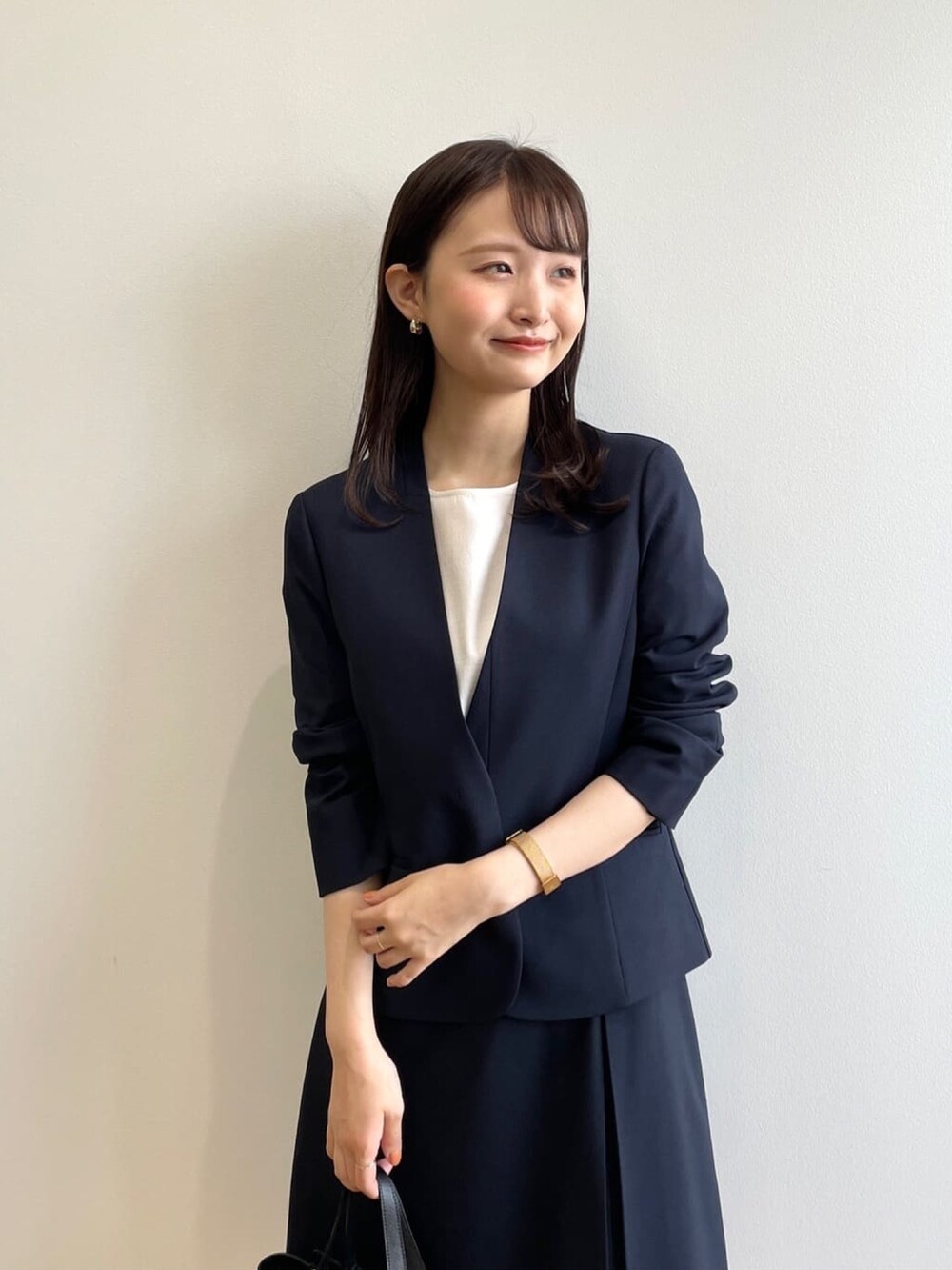 ブラック系のハンドバッグ、ホワイト系のパンプス、ブルー系のノーカラージャケットを着用したレディースの春コーディネートの5枚目の写真