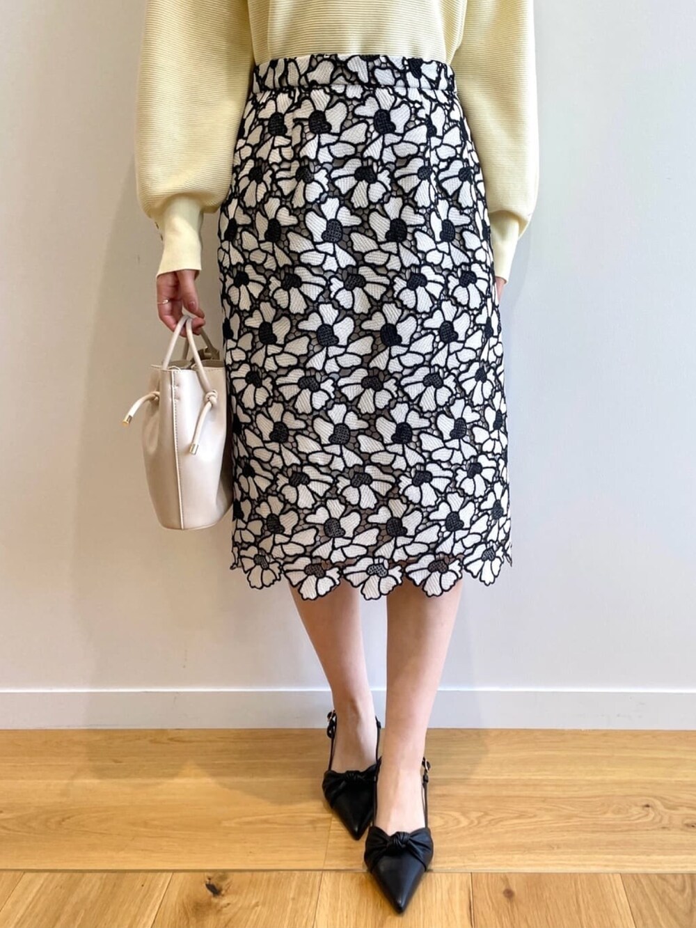 イエロー系のニット/セーター、グレー系のスカート、ホワイト系のショルダーバッグを着用したレディースの春コーディネートの7枚目の写真