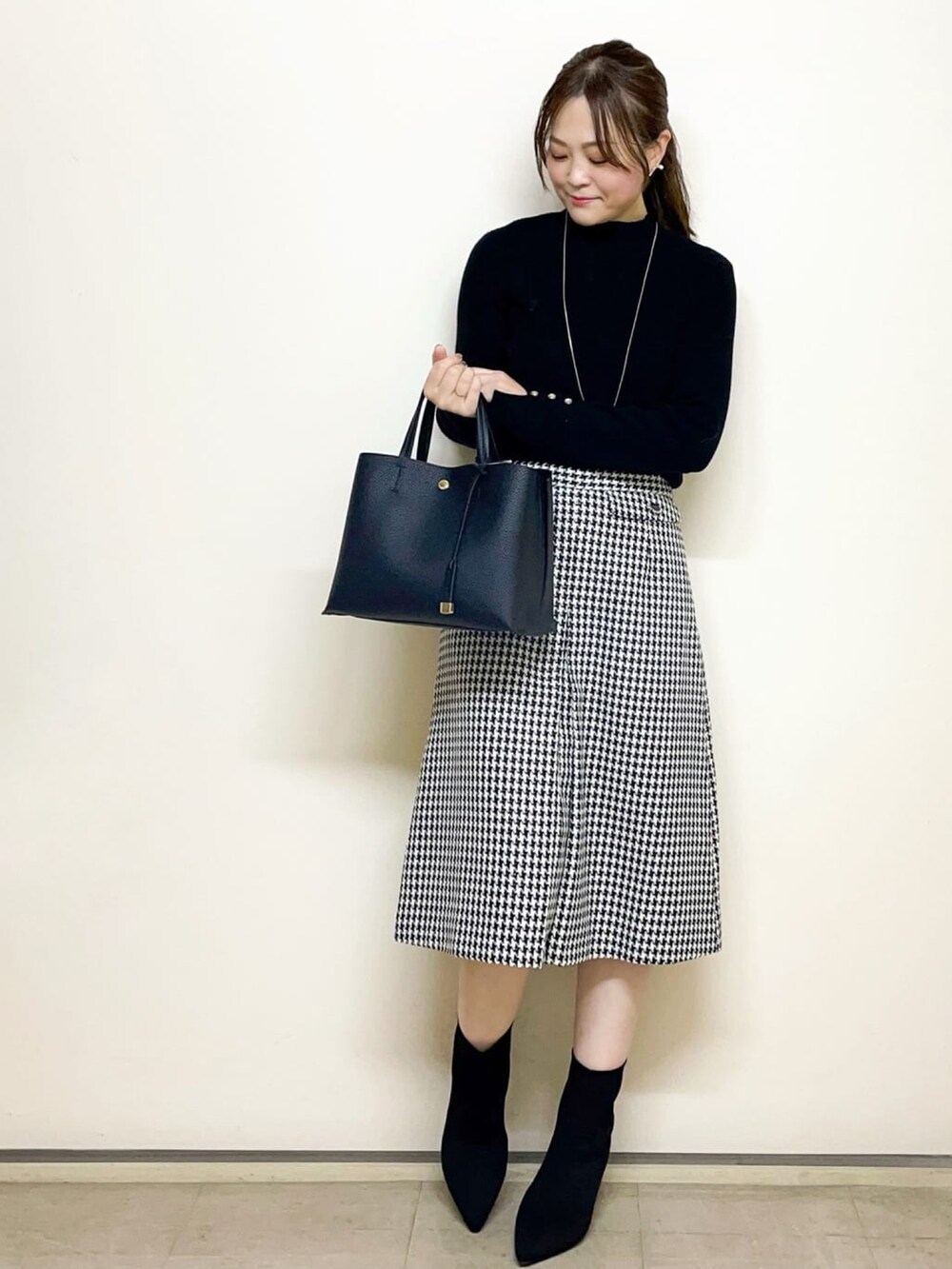 ベージュ系のノーカラーコート、ブラック系のニット/セーター、ブラック系のトートバッグを着用したレディースの冬コーディネートの3枚目の写真