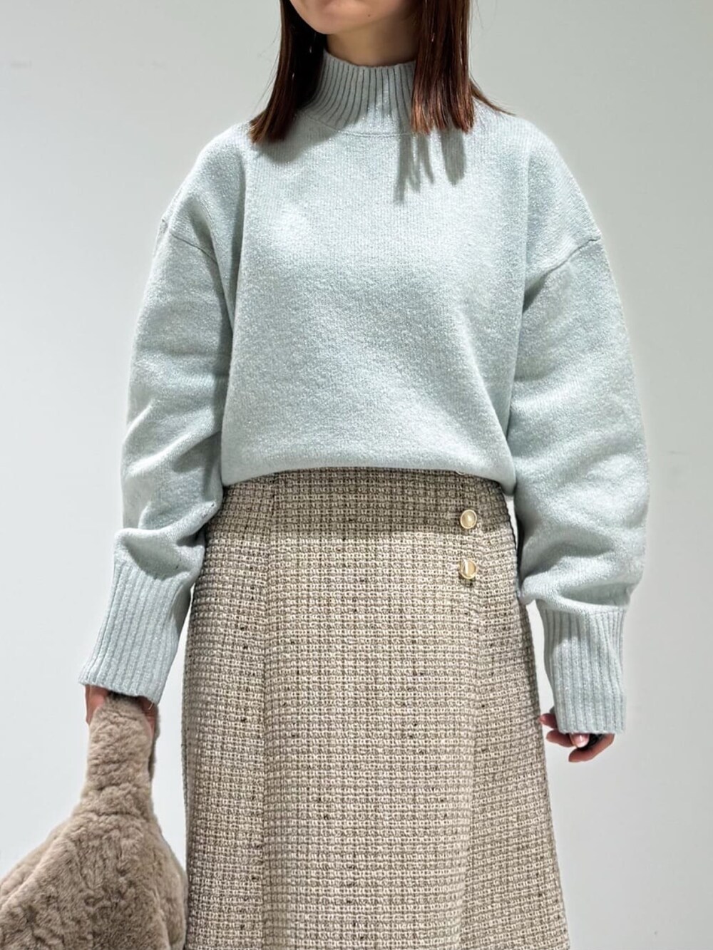 グリーン系のニット/セーター、グレー系のスカート、ベージュ系のハンドバッグを着用したレディースの冬コーディネートの3枚目の写真