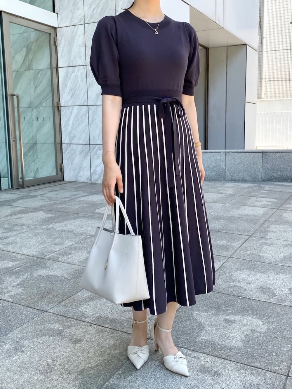 グレー系のワンピース、ホワイト系のパンプス、グレー系のトートバッグを着用したレディースの夏コーディネートの5枚目の写真