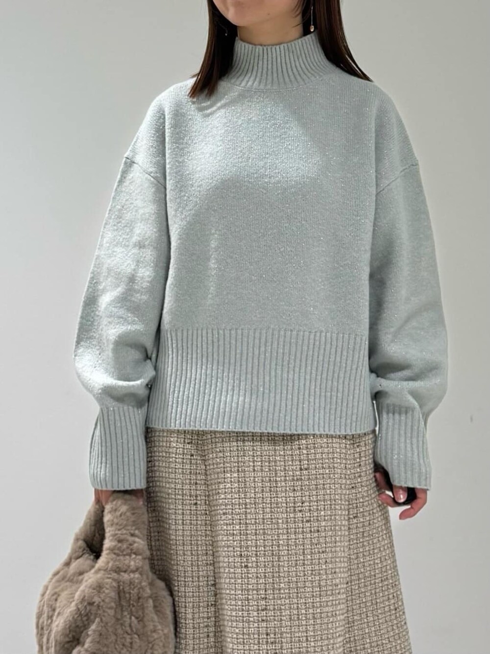 グリーン系のニット/セーター、グレー系のスカート、ベージュ系のハンドバッグを着用したレディースの冬コーディネートの4枚目の写真