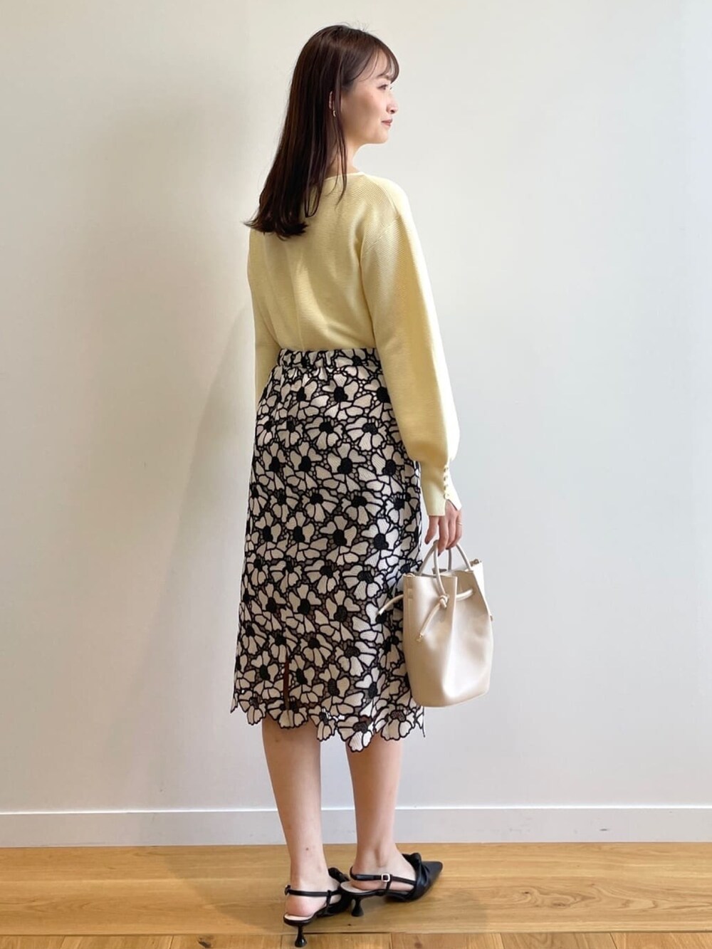 イエロー系のニット/セーター、グレー系のスカート、ホワイト系のショルダーバッグを着用したレディースの春コーディネートの3枚目の写真