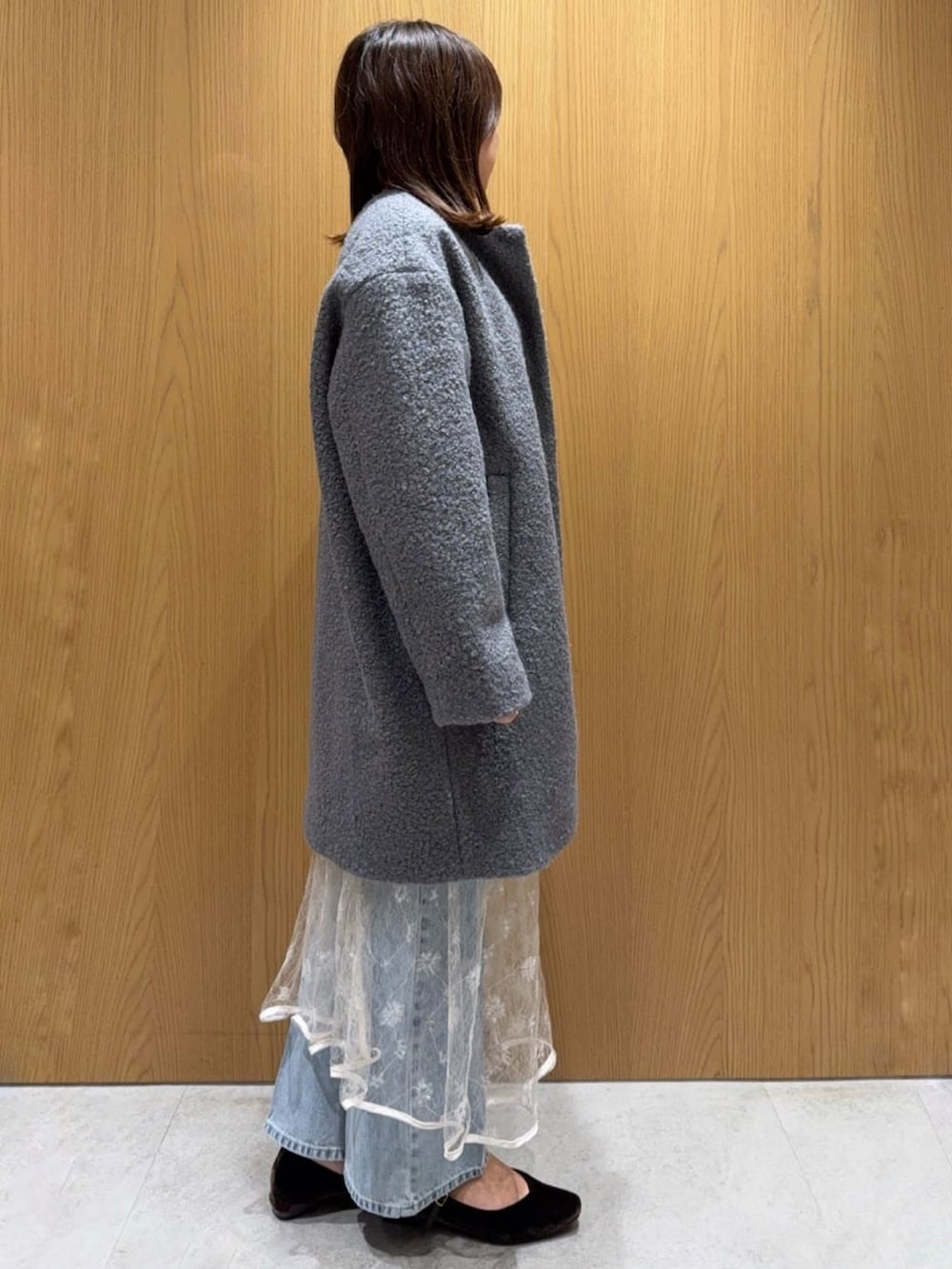 グレー系のノーカラーコート、ホワイト系のカーディガン/ボレロ、ホワイト系のスカートを着用したレディースの秋コーディネートの2枚目の写真