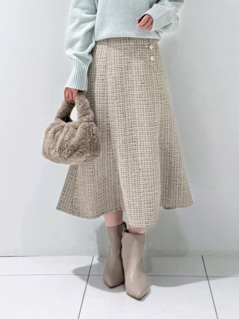 グリーン系のニット/セーター、グレー系のスカート、ベージュ系のハンドバッグを着用したレディースの冬コーディネートの5枚目の写真