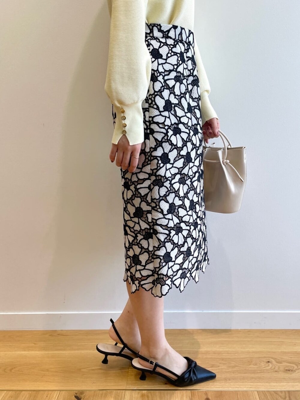 イエロー系のニット/セーター、グレー系のスカート、ホワイト系のショルダーバッグを着用したレディースの春コーディネートの8枚目の写真