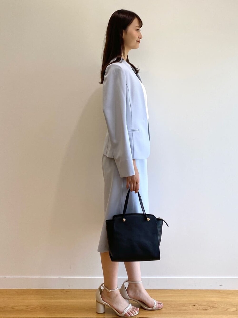 ブルー系のノーカラージャケット、ブルー系のスカート、ブラック系のハンドバッグを着用したレディースの春コーディネートの2枚目の写真