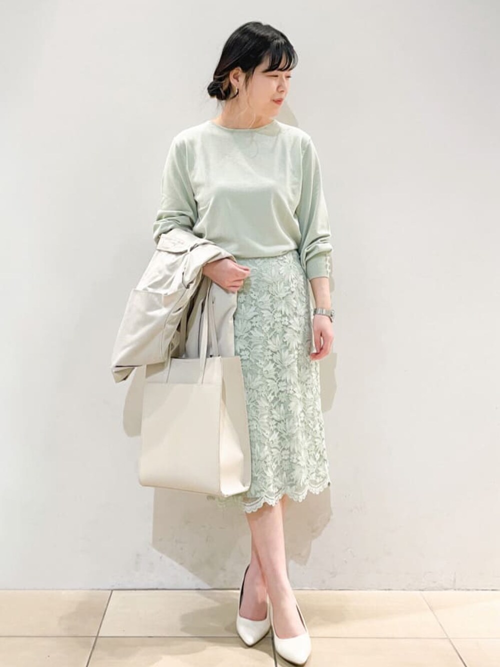 グレー系のトレンチコート、グリーン系のニット/セーター、グリーン系のスカートを着用したレディースの春コーディネートの2枚目の写真