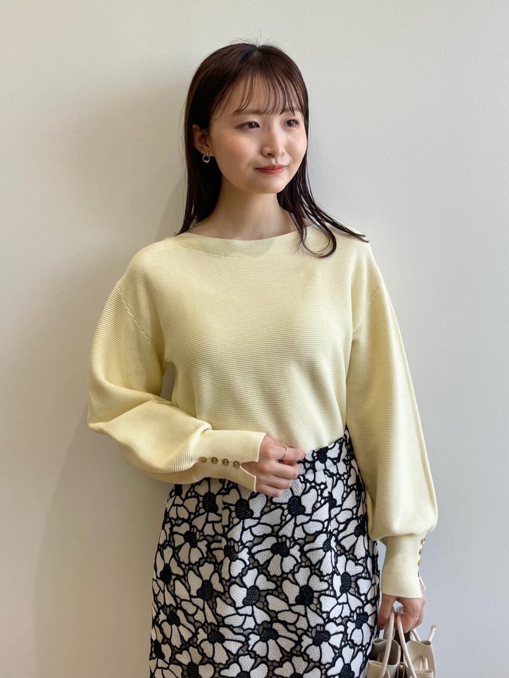 イエロー系のニット/セーター、グレー系のスカート、ホワイト系のショルダーバッグを着用したレディースの春コーディネートの4枚目の写真