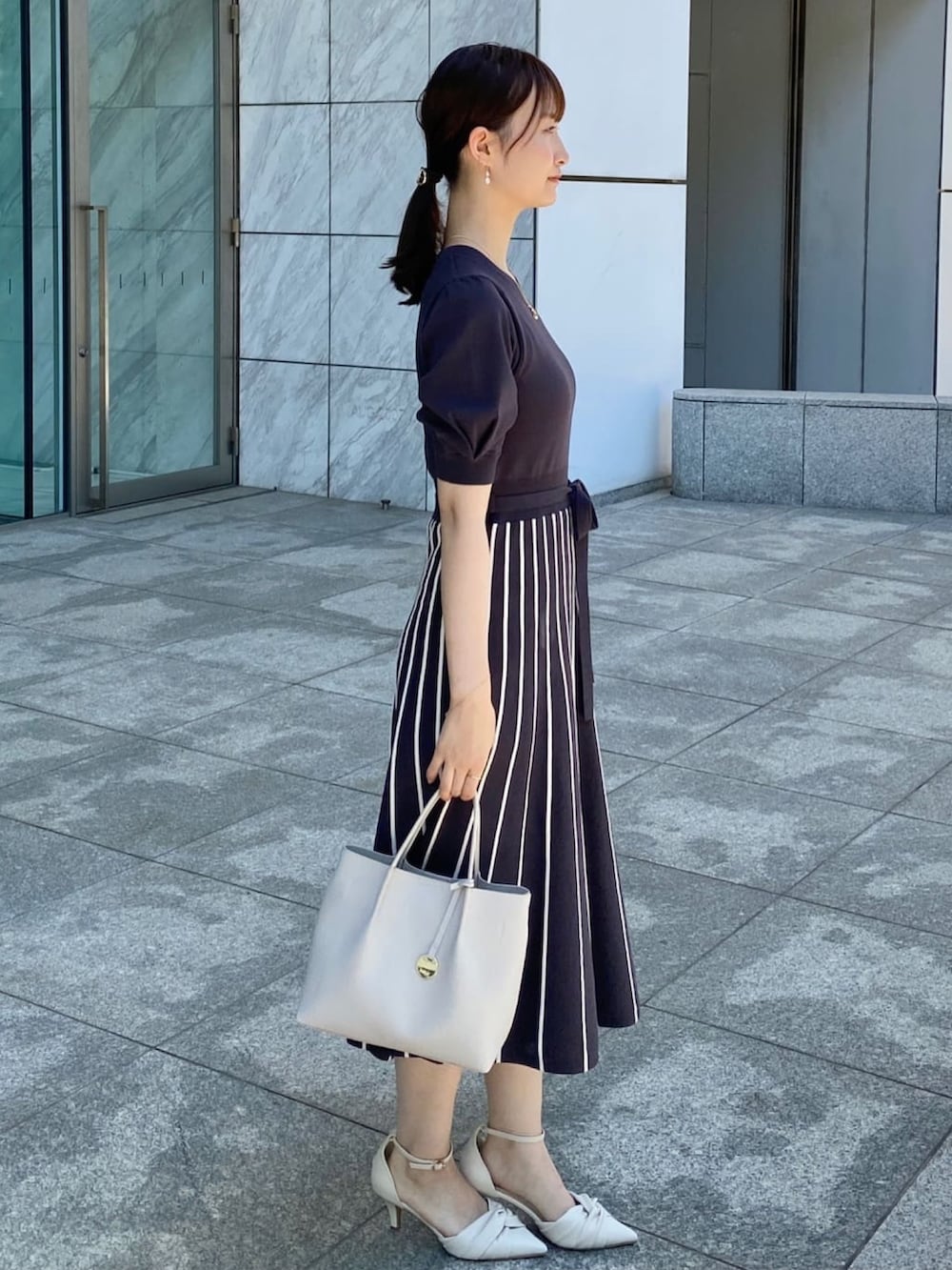 グレー系のワンピース、ホワイト系のパンプス、グレー系のトートバッグを着用したレディースの夏コーディネートの2枚目の写真