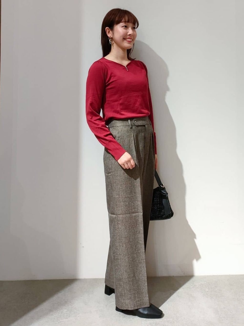 レッド系のニット/セーター、ブラウン系のその他パンツ、ブラック系のショルダーバッグを着用したレディースの秋コーディネートの3枚目の写真