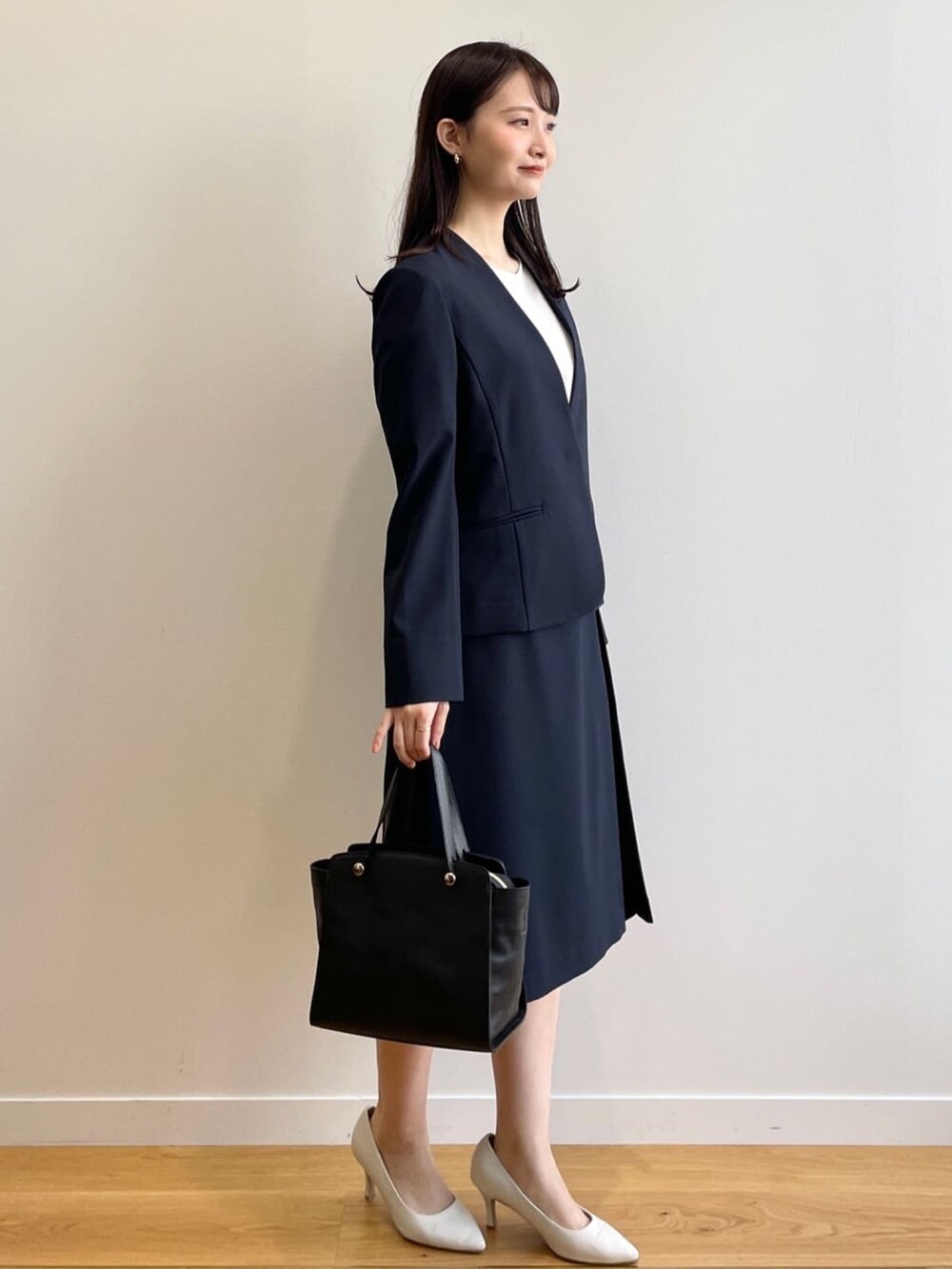 ブラック系のハンドバッグ、ホワイト系のパンプス、ブルー系のノーカラージャケットを着用したレディースの春コーディネートの2枚目の写真