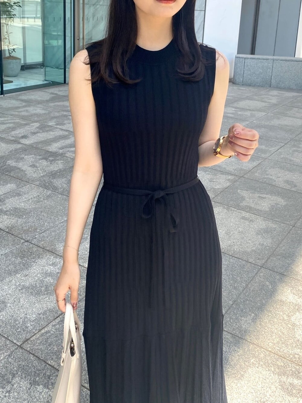 ブラック系のワンピース、ブラック系のパンプス、ゴールド系のピアス（両耳用）を着用したレディースの春コーディネートの4枚目の写真