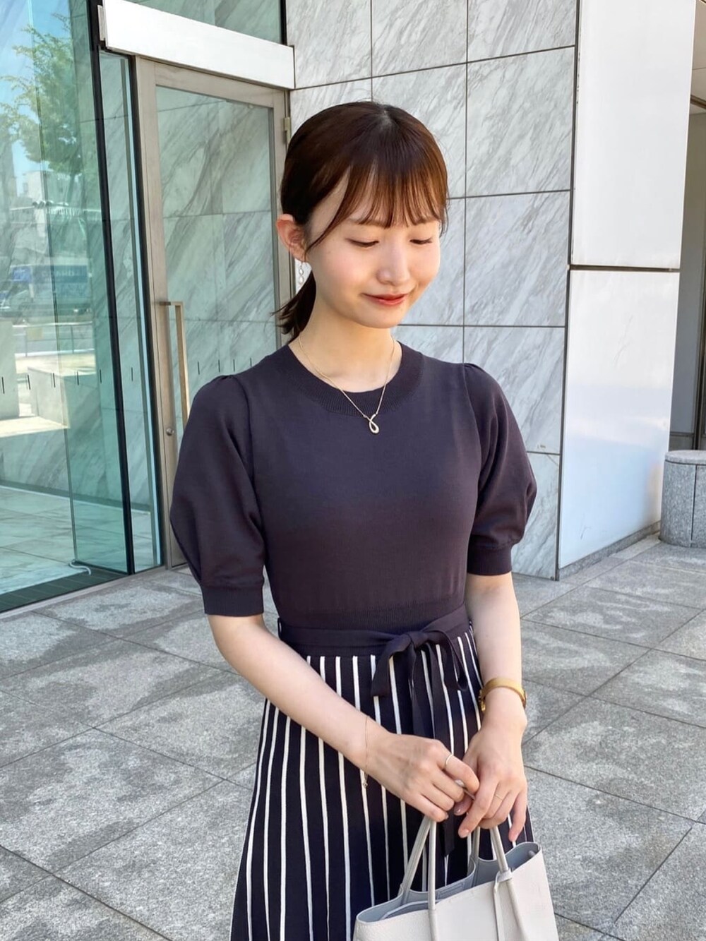 グレー系のワンピース、ホワイト系のパンプス、グレー系のトートバッグを着用したレディースの夏コーディネートの4枚目の写真