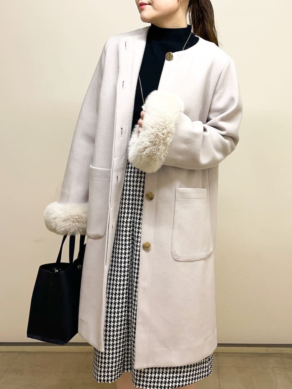 ベージュ系のノーカラーコート、ブラック系のニット/セーター、ブラック系のトートバッグを着用したレディースの冬コーディネートの2枚目の写真