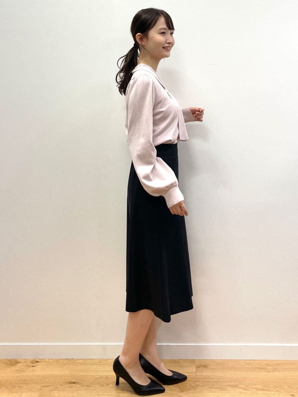 ピンク系のニット/セーター、ブラック系のスカート、ブラック系のパンプスを着用したレディースの秋コーディネートの2枚目の写真