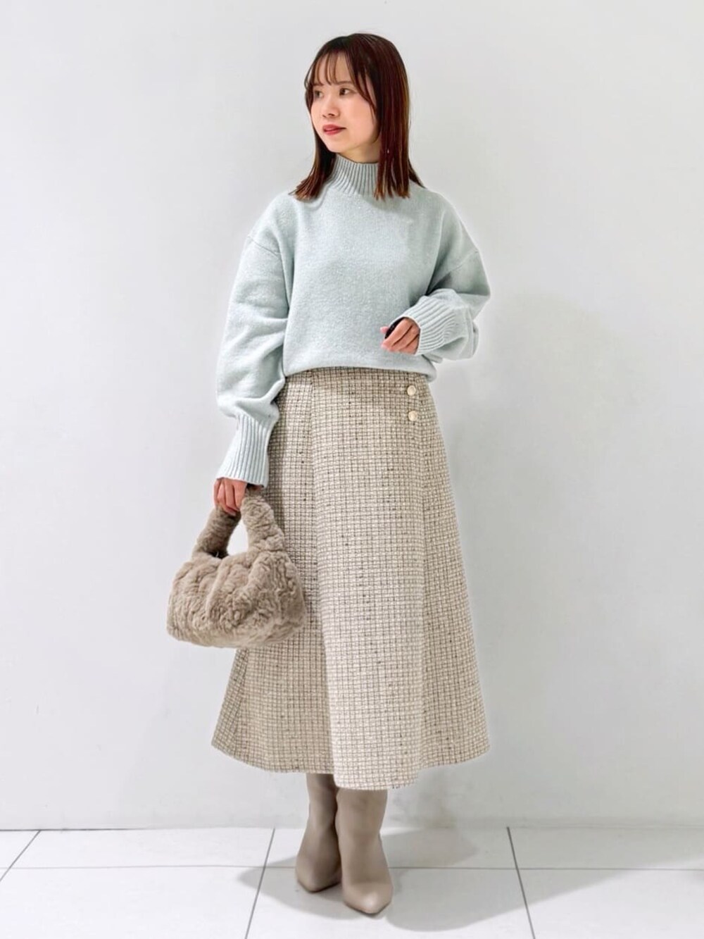 グリーン系のニット/セーター、グレー系のスカート、ベージュ系のハンドバッグを着用したレディースの冬コーディネートの2枚目の写真