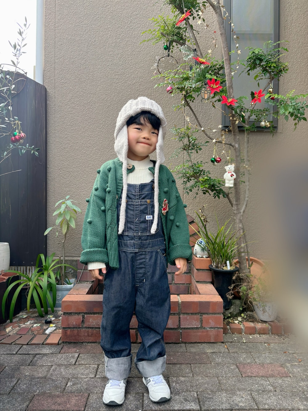 ブルー系のサロペット/オーバーオール、グリーン系のカーディガン/ボレロ、ホワイト系のスニーカーを着用したキッズの冬コーディネートの2枚目の写真