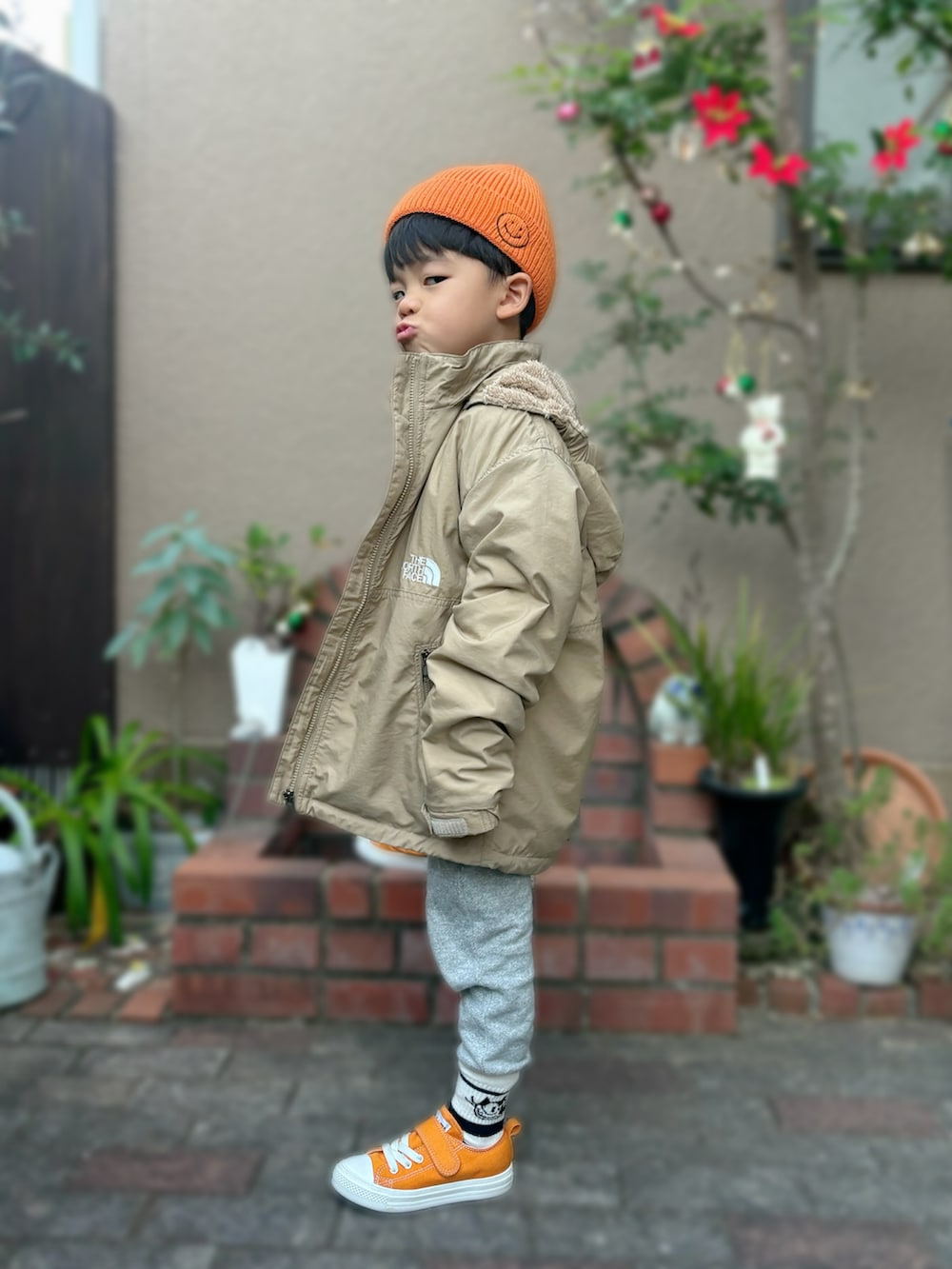 ベージュ系のナイロンジャケット、ブラック系のスウェット、オレンジ系のスニーカーを着用したキッズの秋コーディネートの2枚目の写真