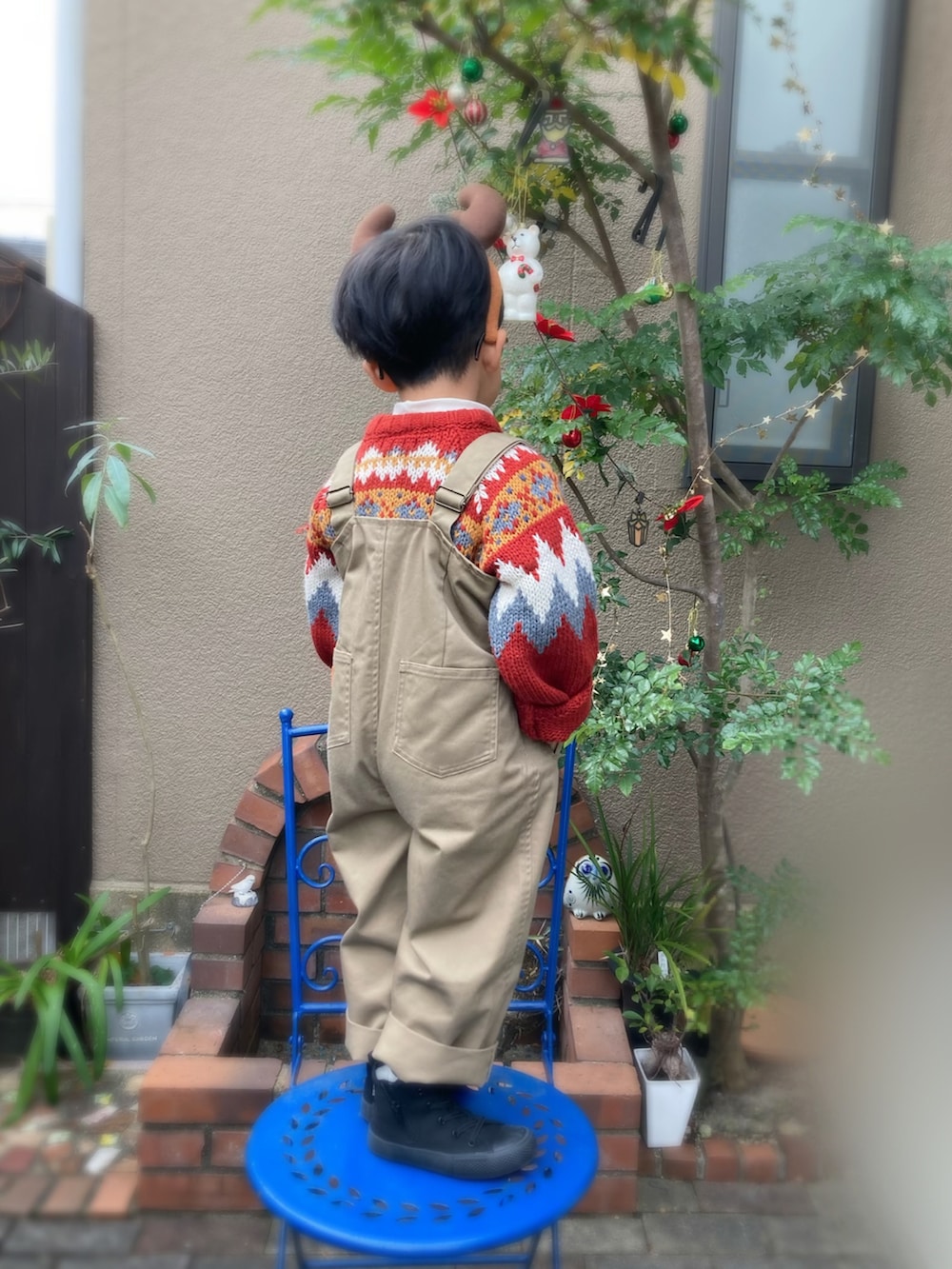 レッド系のニット/セーター、ベージュ系のサロペット/オーバーオール、ブラック系のスニーカーを着用したキッズの冬コーディネートの3枚目の写真