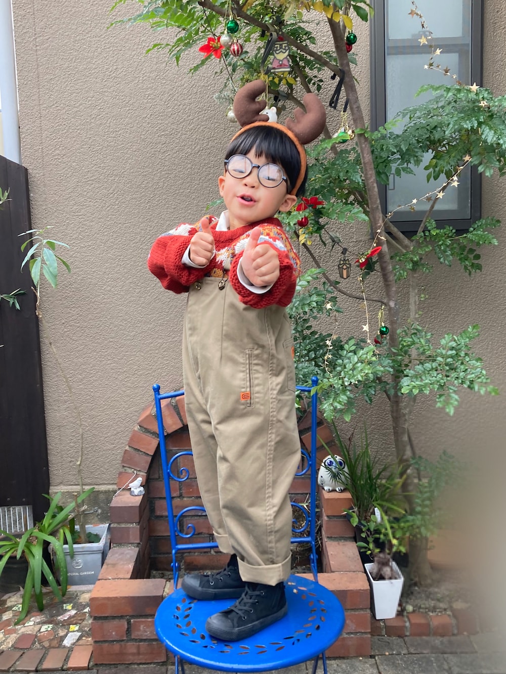 レッド系のニット/セーター、ベージュ系のサロペット/オーバーオール、ブラック系のスニーカーを着用したキッズの冬コーディネートの2枚目の写真