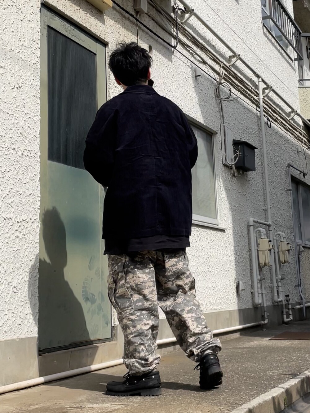 ブラック系のその他シューズ、グリーン系のカーゴパンツ、ブラック系のTシャツ/カットソーを着用したメンズの春コーディネートの2枚目の写真