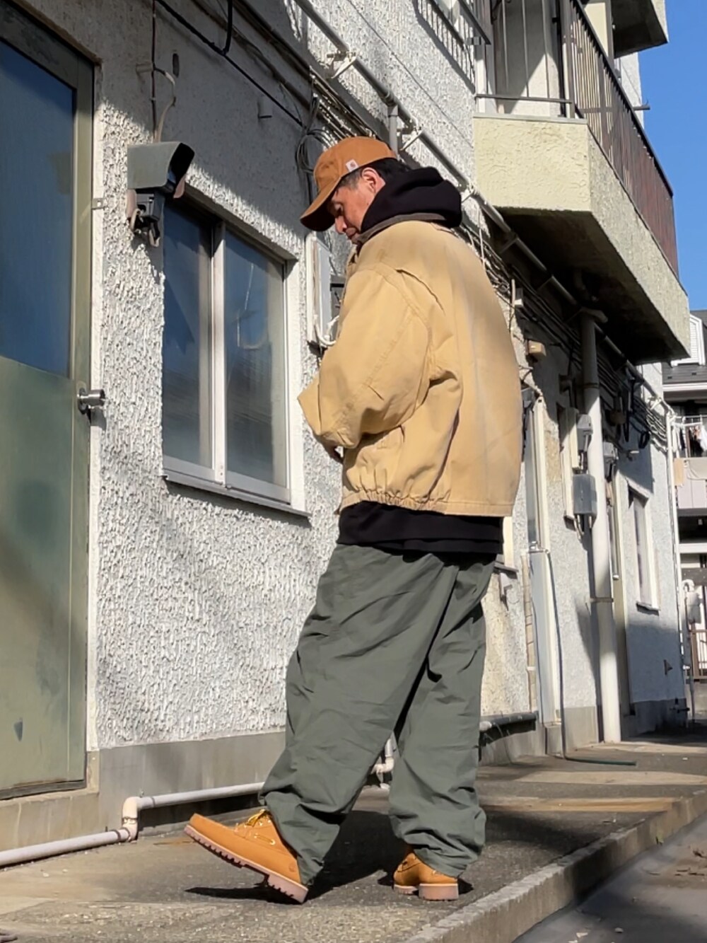 イエロー系のブーツ、グリーン系のパンツ、ブラック系のパーカーを着用したメンズの冬コーディネートの2枚目の写真