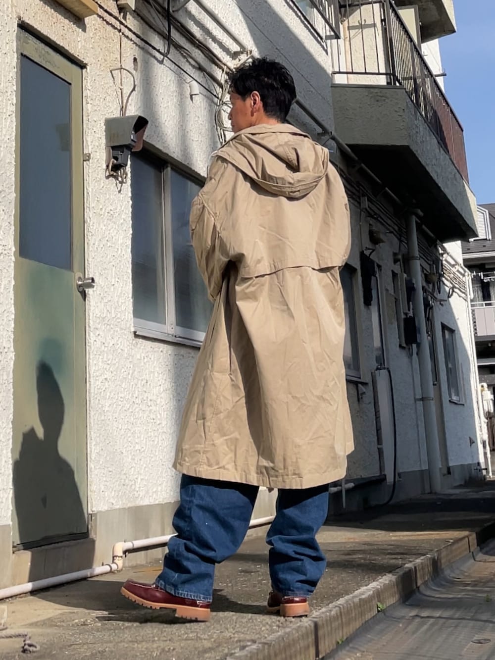 ベージュ系のステンカラーコート、ブルー系のデニムパンツ、ブラウン系のニット/セーターを着用したメンズの春コーディネートの2枚目の写真