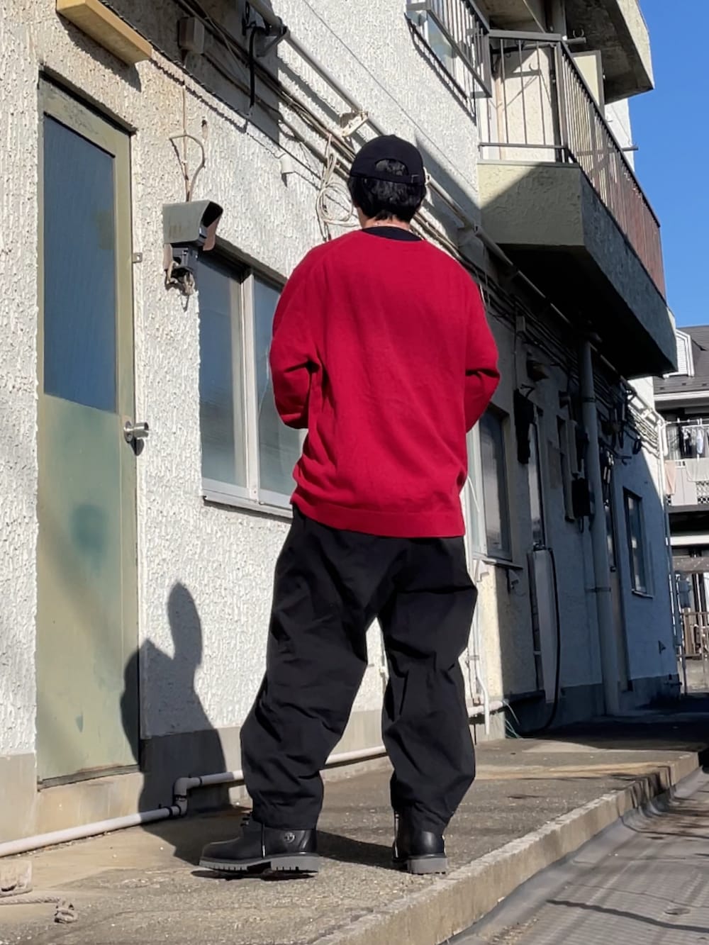 レッド系のニット/セーター、ブラック系のブーツ、ブラック系のパンツを着用したメンズの冬コーディネートの2枚目の写真