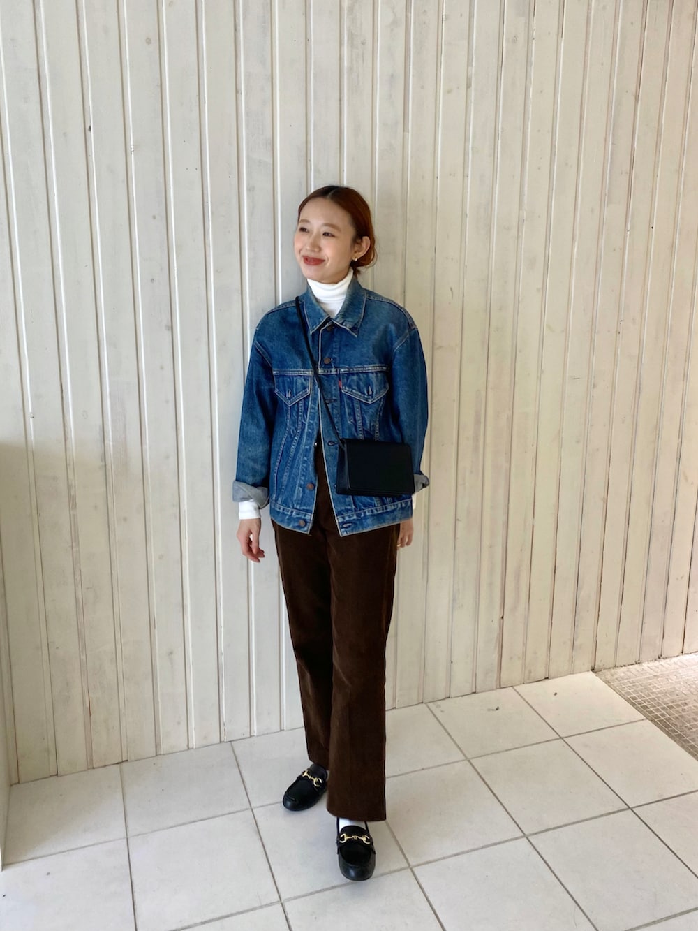 ブルー系のデニムジャケット、ブラウン系のパンツ、ブラック系のショルダーバッグを着用したレディースの冬コーディネートの2枚目の写真