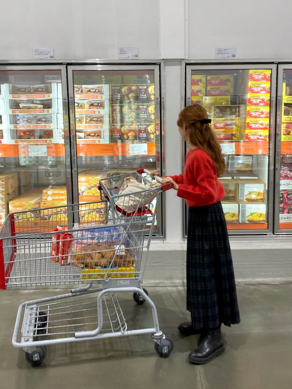 レッド系のニット/セーター、グリーン系のスカート、ブラック系のブーツを着用したレディースの冬コーディネートの2枚目の写真