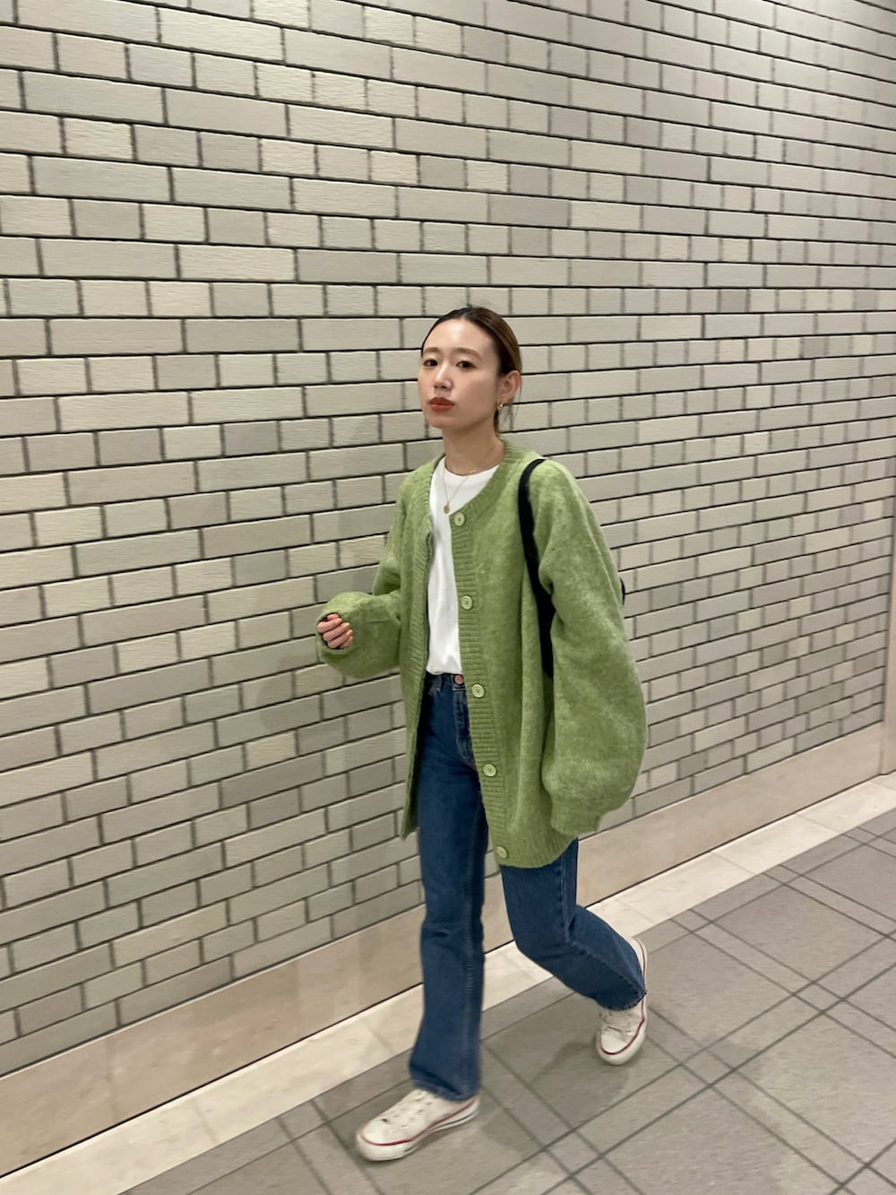 グリーン系のカーディガン/ボレロ、ブラック系のハンドバッグ、ブルー系のデニムパンツを着用したレディースの冬コーディネートの3枚目の写真