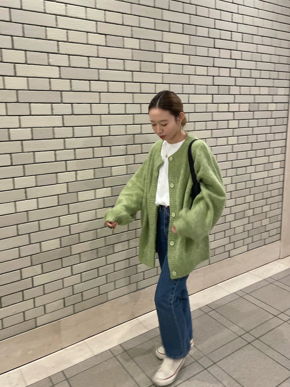 グリーン系のカーディガン/ボレロ、ブラック系のハンドバッグ、ブルー系のデニムパンツを着用したレディースの冬コーディネートの2枚目の写真