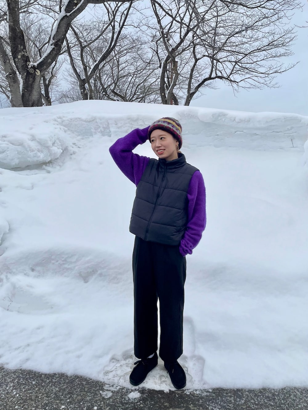 パープル系のニット/セーター、ブラック系のベスト、ブラック系のシューズを着用したレディースの冬コーディネートの2枚目の写真