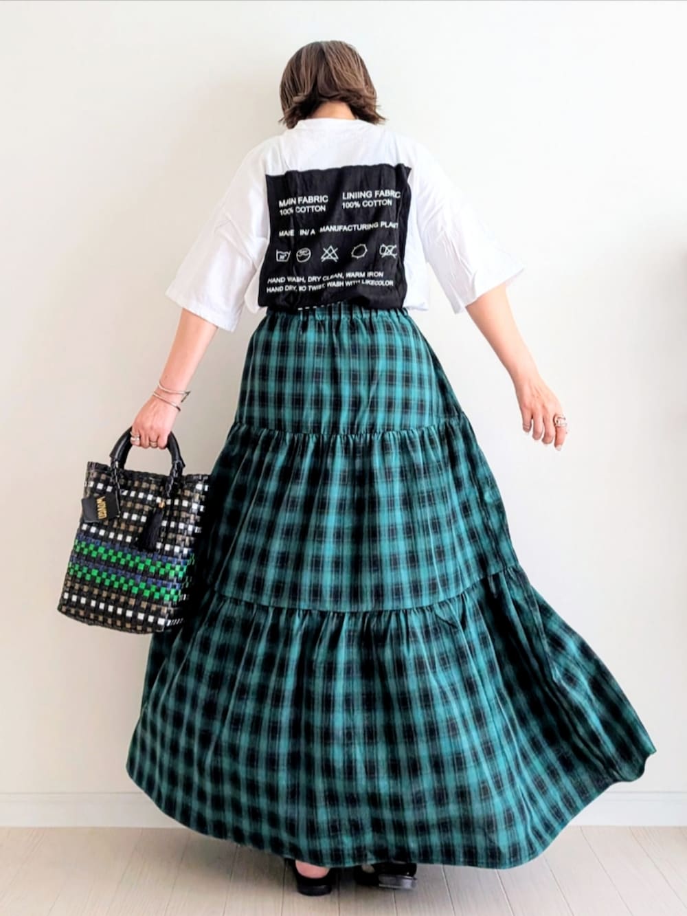 グリーン系のスカート、ブラック系のかごバッグ、ホワイト系のTシャツ/カットソーを着用したレディースの春コーディネートの2枚目の写真