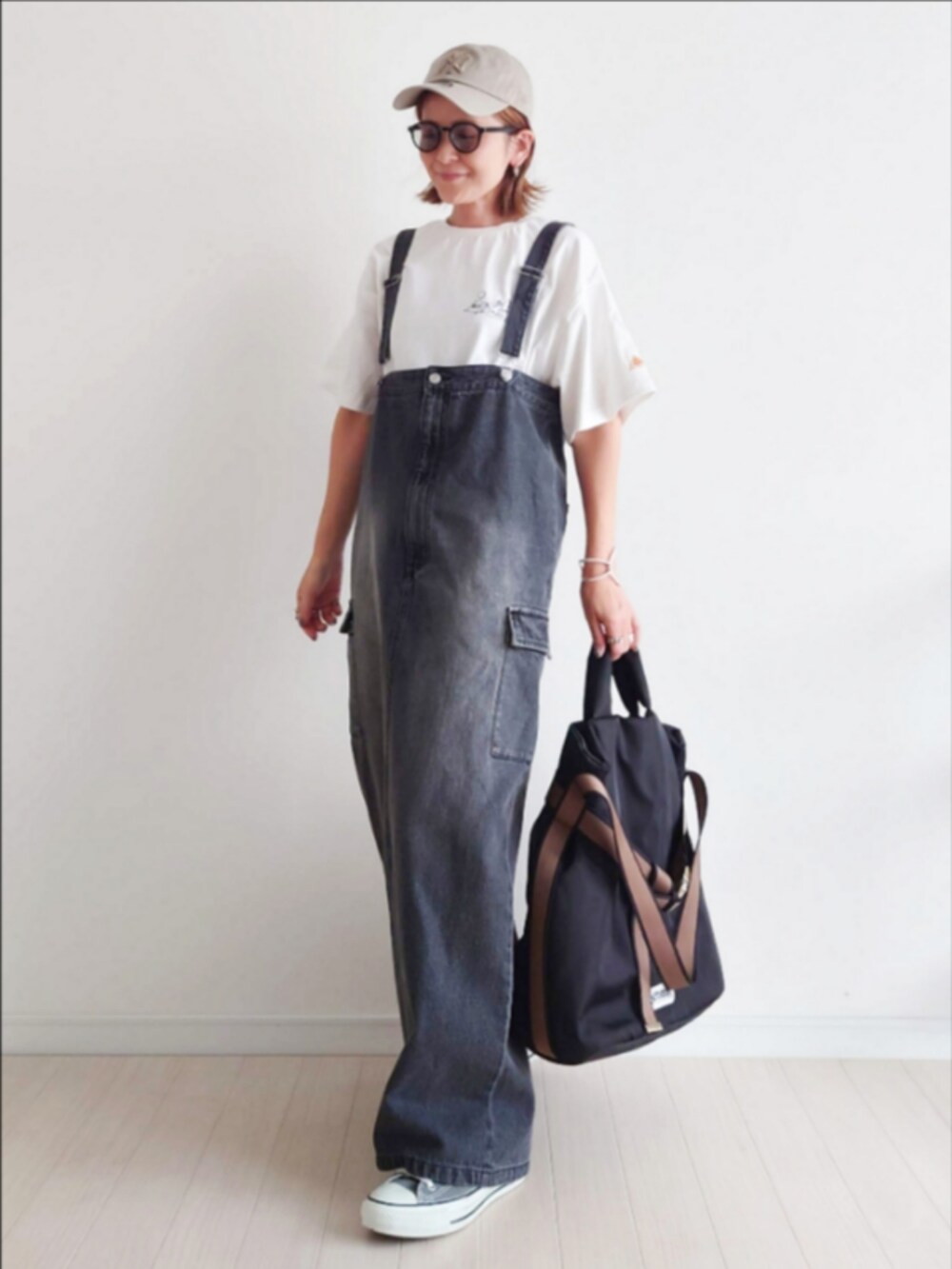 ブラック系のジャンパースカート、ホワイト系のTシャツ/カットソー、ブラック系のトートバッグを着用したレディースの秋コーディネートの3枚目の写真