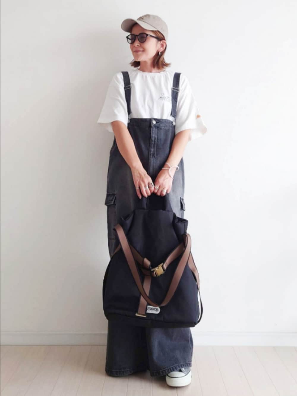 ブラック系のジャンパースカート、ホワイト系のTシャツ/カットソー、ブラック系のトートバッグを着用したレディースの秋コーディネートの2枚目の写真