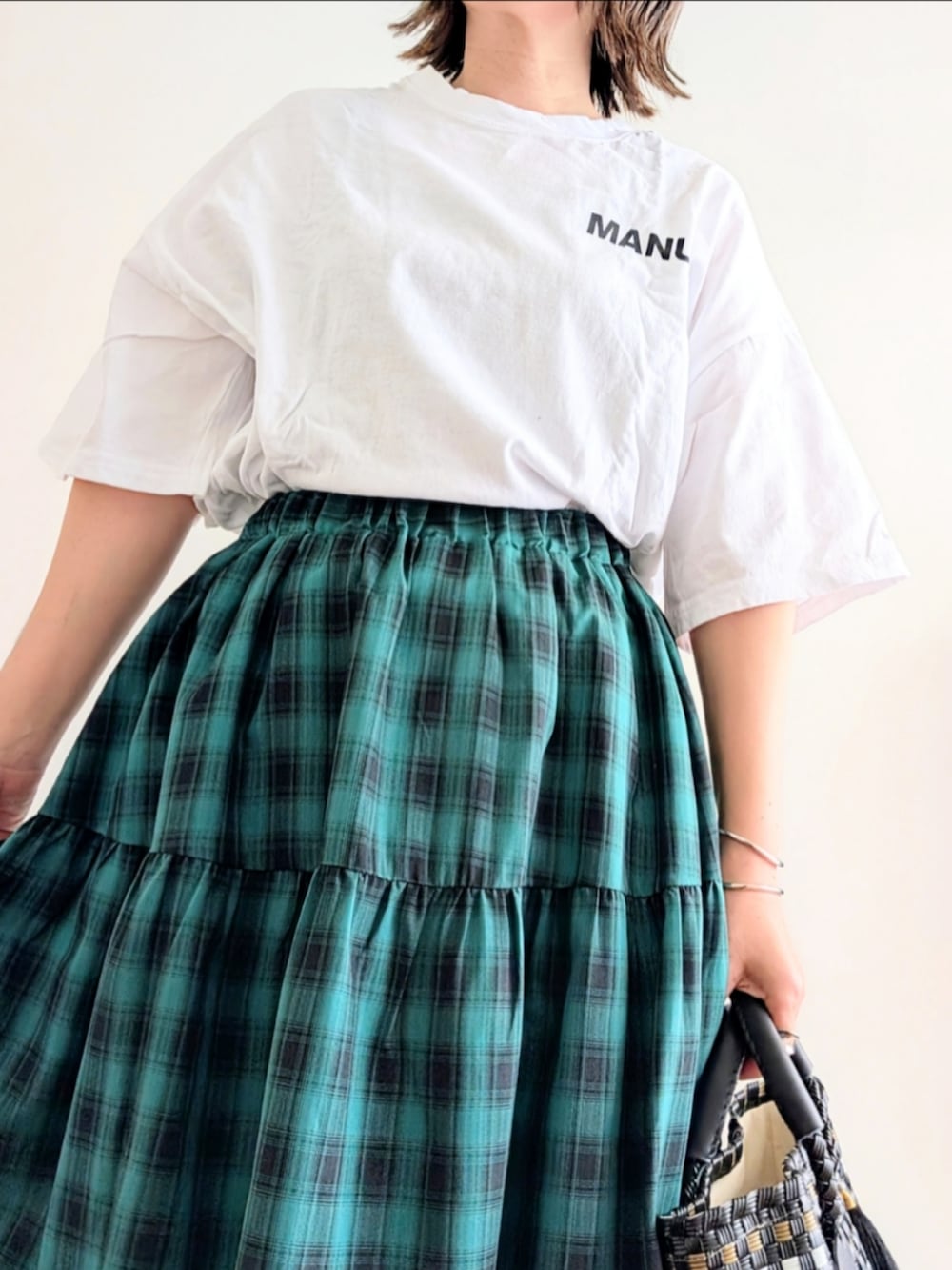 グリーン系のスカート、ブラック系のかごバッグ、ホワイト系のTシャツ/カットソーを着用したレディースの春コーディネートの4枚目の写真