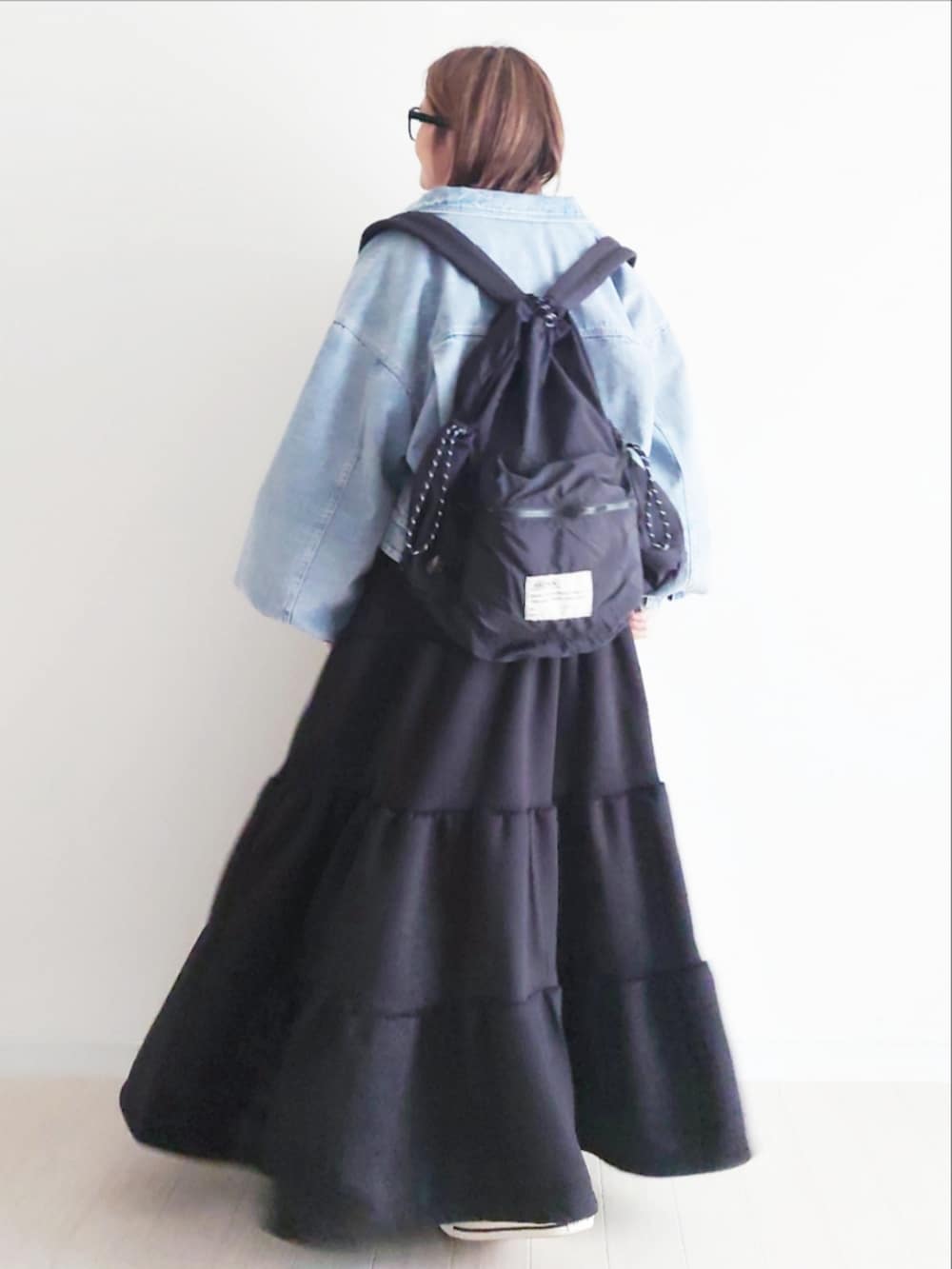ブルー系のデニムジャケット、ブラック系のバックパック/リュック、ブラック系のワンピースを着用したレディースの冬コーディネートの2枚目の写真