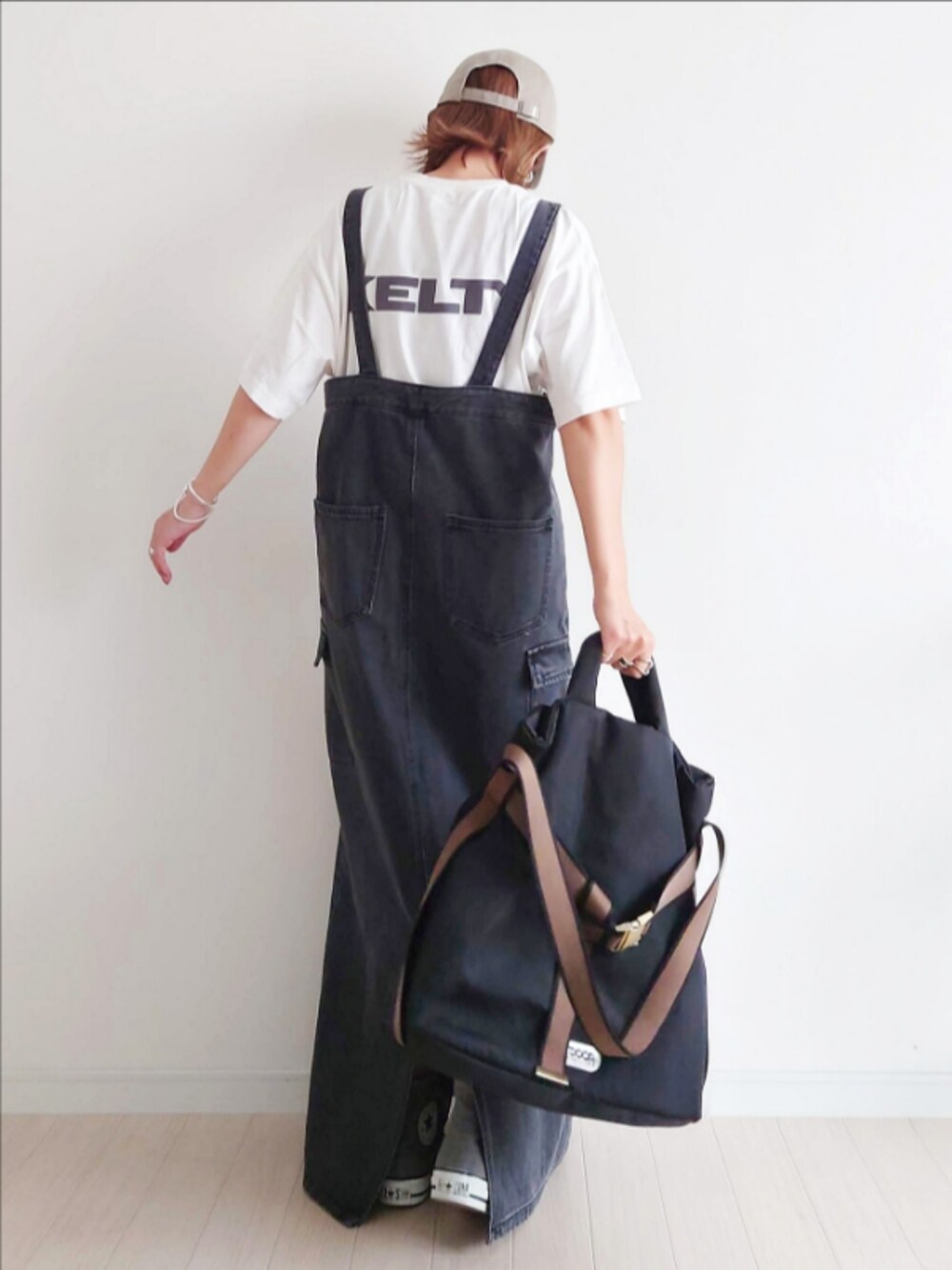 ブラック系のジャンパースカート、ホワイト系のTシャツ/カットソー、ブラック系のトートバッグを着用したレディースの秋コーディネートの4枚目の写真