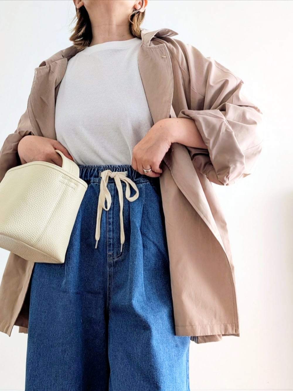 ブルー系のデニムパンツ、ベージュ系のトレンチコート、ホワイト系のスニーカーを着用したレディースの春コーディネートの5枚目の写真