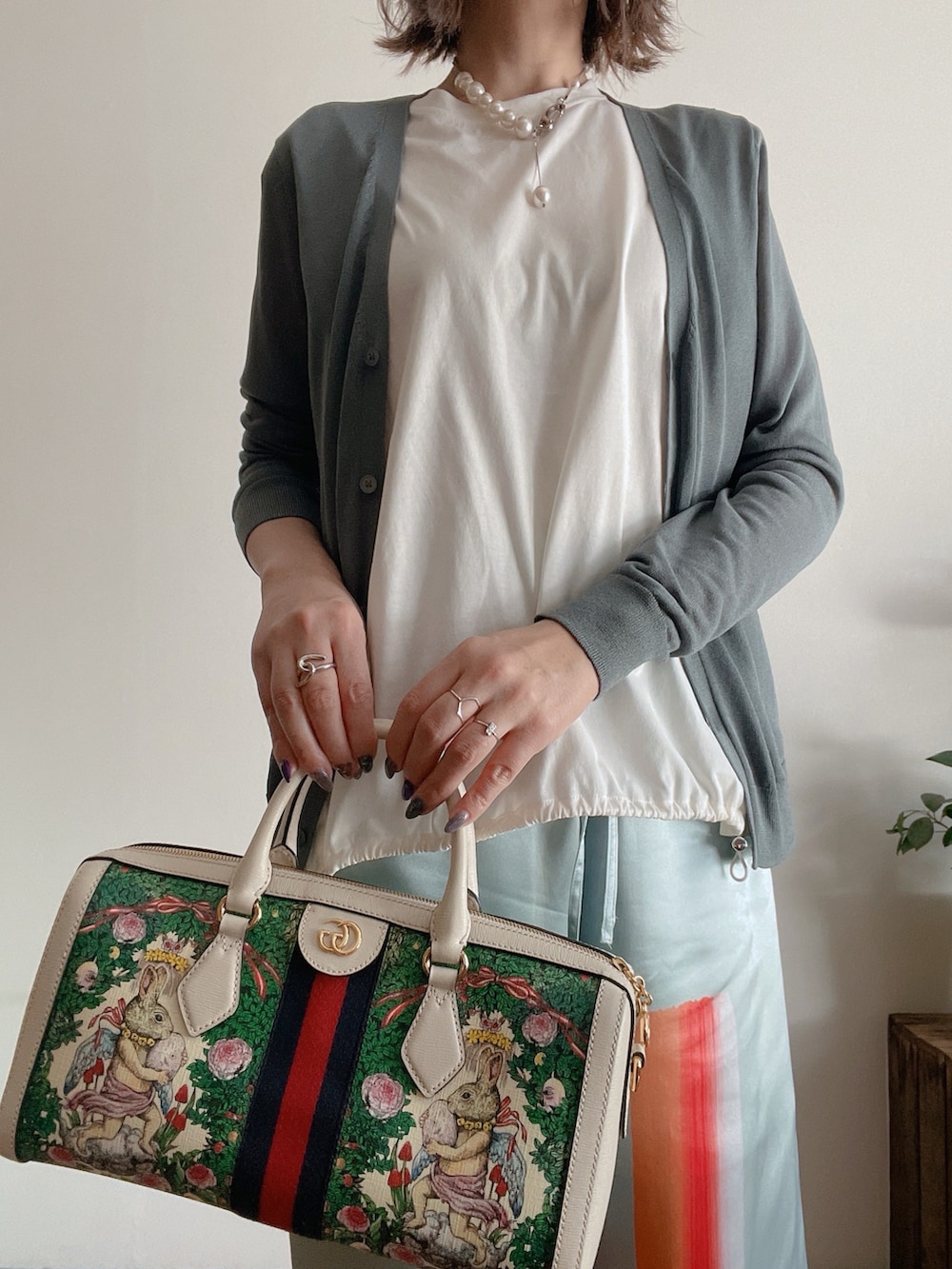 グリーン系のカーディガン/ボレロ、ブルー系のパンツ、シルバー系のネックレスを着用したレディースの春コーディネートの2枚目の写真