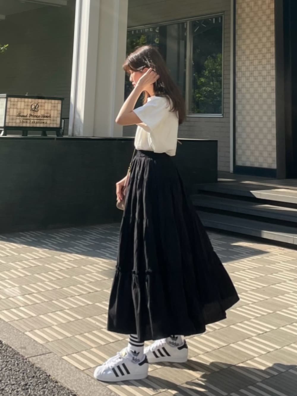 ブラック系のスカート、ホワイト系のTシャツ/カットソー、ホワイト系のスニーカーを着用したレディースの秋コーディネートの2枚目の写真