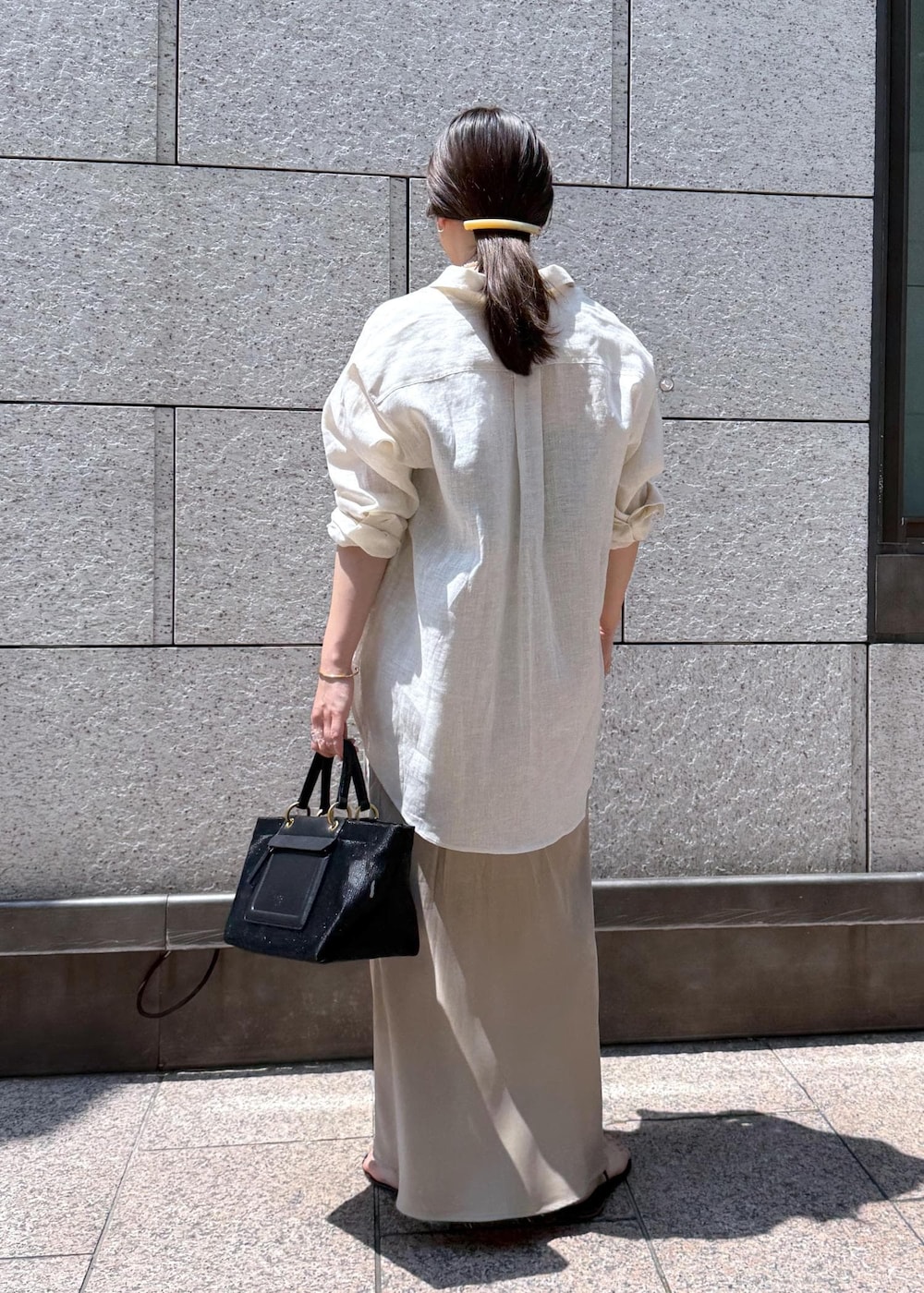 ブラック系のハンドバッグ、ベージュ系のスカート、ホワイト系のシャツ/ブラウスを着用したレディースの夏コーディネートの2枚目の写真