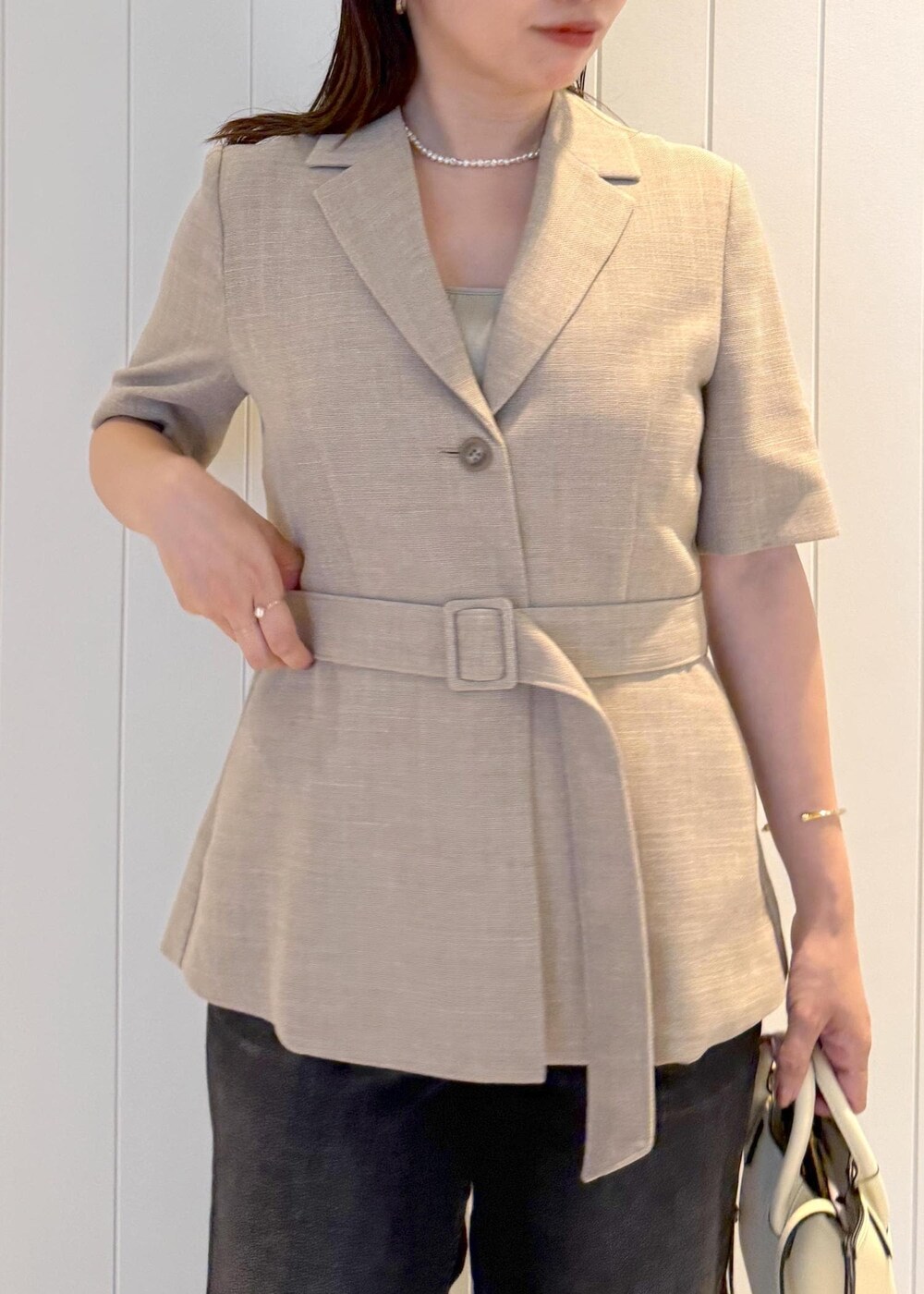 ベージュ系のテーラードジャケット、ブラック系のデニムパンツ、ホワイト系のショルダーバッグを着用したレディースの夏コーディネートの4枚目の写真