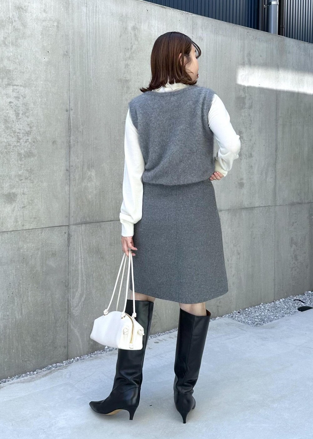 ブラック系のブーツ、ホワイト系のハンドバッグ、グレー系のベストを着用したレディースの秋コーディネートの3枚目の写真
