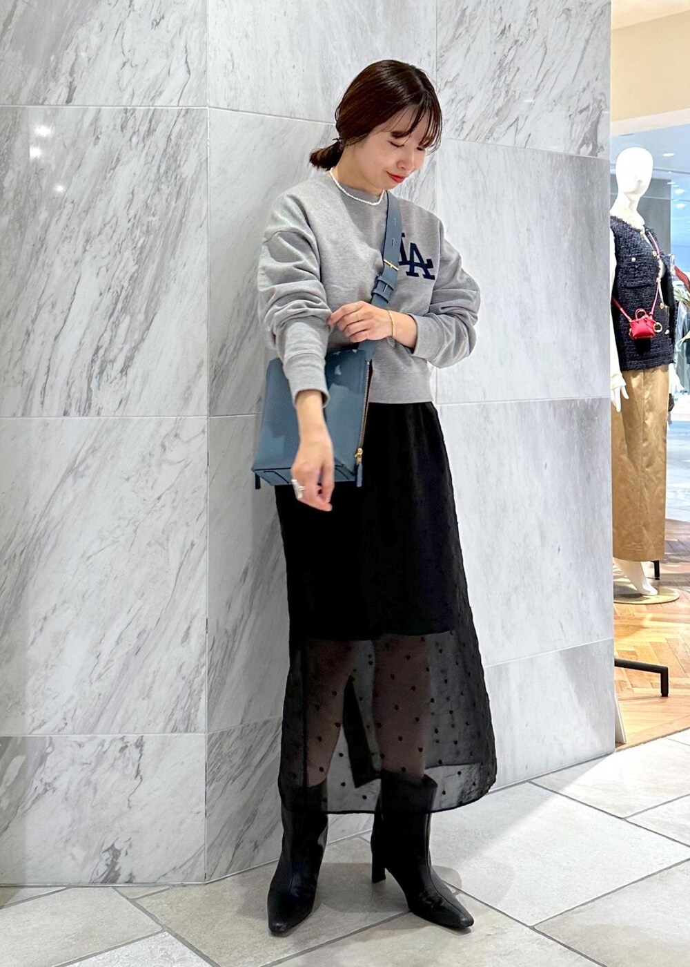 グレー系のスウェット、ブルー系のショルダーバッグ、ブラック系のスカートを着用したレディースの秋コーディネートの2枚目の写真