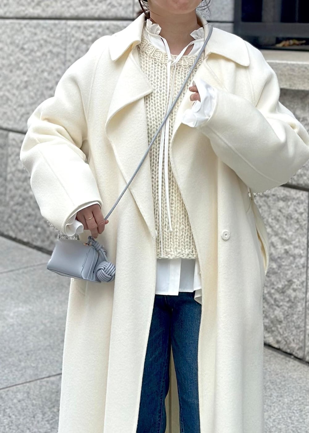 ブルー系のショルダーバッグ、ホワイト系のチェスターコート、ホワイト系のニット/セーターを着用したレディースの冬コーディネートの4枚目の写真